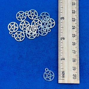 Puede incluir: Un grupo de dijes pentagrama de color plateado, de aproximadamente 2,5 cm de diámetro, sobre un fondo azul. Se incluye una regla para la escala.