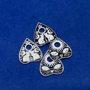 May include: Four black and white metal charms shaped like a witch's board planchette. Each charm features a different design with a cat, moon, and stars.