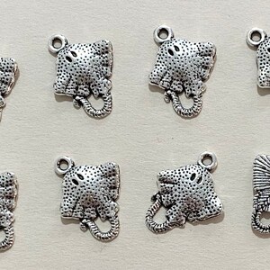 Op de afbeelding: Acht zilverkleurige metalen bedels in de vorm van roggen. De bedels hebben een getextureerd oppervlak en een lus aan de bovenkant om aan een ketting of armband te bevestigen.