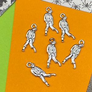 May include: Six silver-toned charms shaped like walking zombies. The charms have a loop at the top for attaching to a necklace or bracelet.