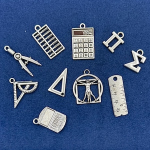 Può includere: Una collezione di ciondoli color argento a forma di calcolatrice, abaco, goniometro, triangolo, righello e laptop. I ciondoli sono sparsi su una superficie blu scuro.