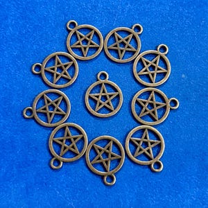 May include: A collection of bronze-colored pentagram charms, each with a loop for attaching to jewelry or other crafts. The charms are arranged on a blue surface.