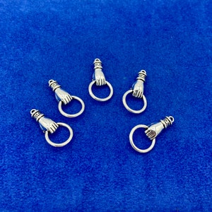Può includere: Cinque ciondoli in argento a forma di mano con un anello. I ciondoli sono su uno sfondo blu.
