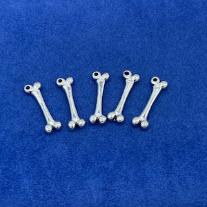 Puede incluir: Seis abalorios de hueso de plata con extremos redondeados. Los abalorios miden aproximadamente 2,5 cm de largo y tienen un bucle en la parte superior para sujetarlos a un collar o pulsera.