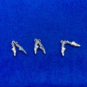Puede incluir: Tres abalorios de zapato de ballet plateados, cada uno con un bucle para sujetar a un collar, pulsera u otra joya.