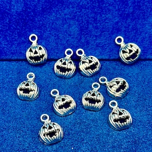 May include: Ten silver charm pendants shaped like jack-o'-lanterns with black face details. The charms have a loop at the top for attaching to a necklace or bracelet.