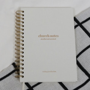 May include: A white spiral bound notebook with the text "church notes" in gold lettering. The notebook has the words "attending and sustained" and "writing & reflection" printed in smaller gold lettering.