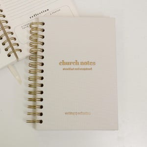 May include: Cream-colored spiral-bound notebook with gold lettering that reads "church notes" and "writing & reflection." The notebook is open to a page with lines and the word "reflection" printed at the top.