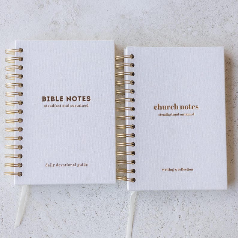 May include: Two white spiral-bound notebooks with gold coils. One notebook reads "BIBLE NOTES" and "daily devotional guide." The other reads "church notes" and "writing & reflection." Both notebooks have the phrase "steadfast and sustained."