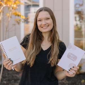 Puede incluir: Una persona sostiene dos cuadernos blancos. El cuaderno de la izquierda tiene encuadernaci&oacute;n en espiral dorada y las palabras "Bible Notes" y "daily devotional plan" impresas en la portada. El cuaderno de la derecha tiene las palabras "Standfast Sustained" en la portada.