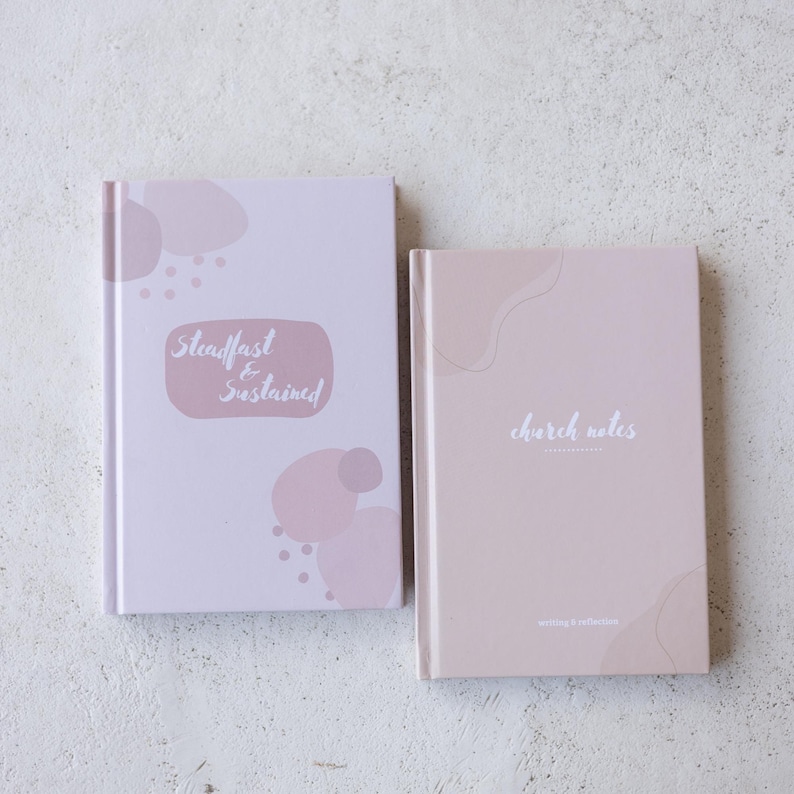 Puede incluir: Dos cuadernos con cubiertas de color rosa p&aacute;lido. El cuaderno m&aacute;s grande tiene las palabras "Steadfast & Sustained" en un &oacute;valo rosa. El cuaderno m&aacute;s peque&ntilde;o tiene las palabras "church notes" en escritura blanca. Ambos cuadernos tienen formas rosas abstractas.