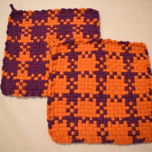 May include: Two woven pot holders in a checkered pattern of orange and purple.