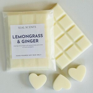 May include: A pack of soy wax melts in a white wrapper with the text "SEAL SCENTS LEMONGRASS & GINGER" and the description "relaxing citrus mixed with spiced herbs and a hint of fresh eucalyptus" and "HAND POURED SOY WAX MELT". The pack is next to a white wax melt bar and three heart-shaped wax melts.