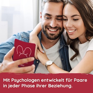 May include: A couple smiles while looking at a red card game with a white outline of two people kissing. The text on the card reads "Intimacy". The text below the image reads "Mit Psychologen entwickelt f&uuml;r Paare in jeder Phase ihrer Beziehung."
