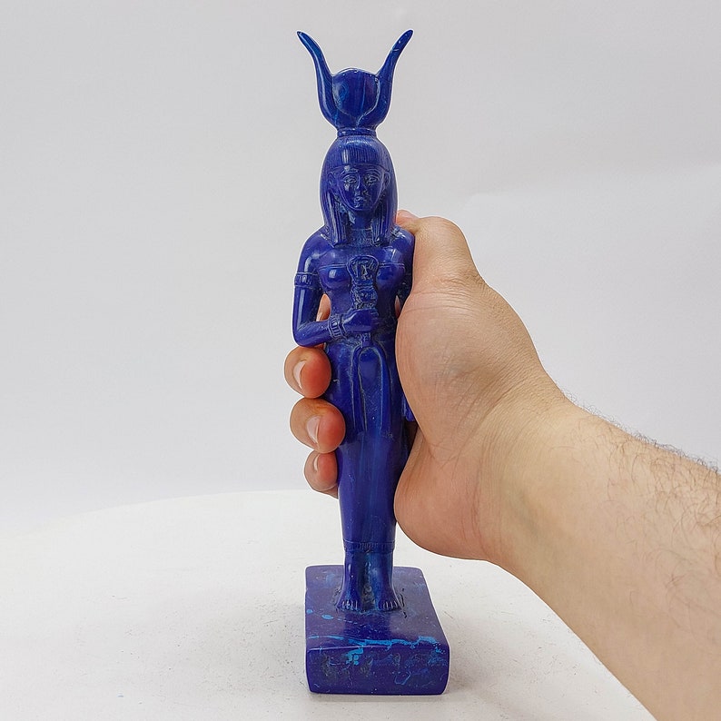 Op de afbeelding: Een blauw lapis lazuli beeld van een Egyptische godin met een kroon en een staf. Het beeld staat op een rechthoekige basis.