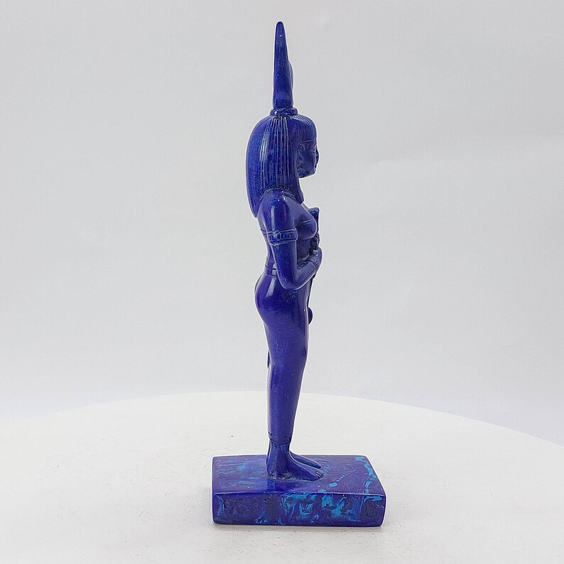 Op de afbeelding: Een blauw lapis lazuli beeldje van een Egyptische godin met een hoge hoofdtooi. Het beeldje staat op een blauw-witte basis.