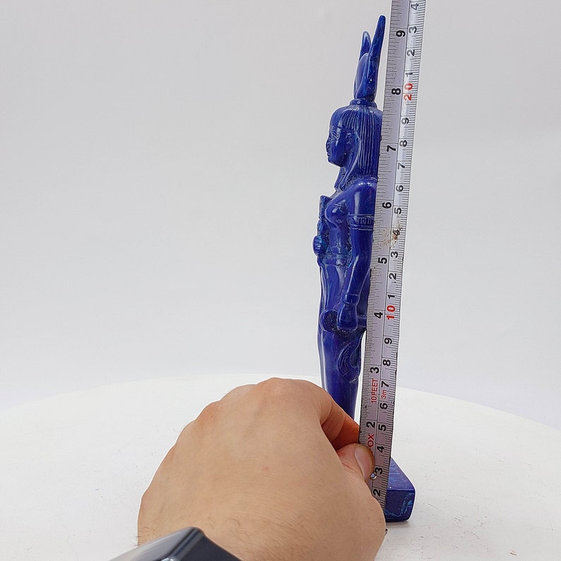 Op de afbeelding: Een blauw lapis lazuli beeld van een Egyptische godin, staand op een kleine basis. Het beeld is ongeveer 19 cm hoog.
