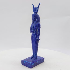 Op de afbeelding: Een blauw lapis lazuli beeld van een Egyptische godin met een hoge hoofdtooi. Het beeld staat op een rechthoekige basis.