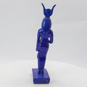 Op de afbeelding: Een blauw lapis lazuli beeld van een Egyptische godin met een hoofdtooi. Het beeld staat op een rechthoekige basis.