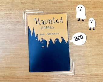 Pode incluir: Um livro amarelo com o título "Haunted Homes for Introverts" e uma silhueta preta de casas. Uma bolha de fala branca com a palavra "BOO" e duas figuras de fantasmas brancos estão do lado direito do livro.