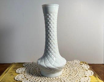 May include: A white milk glass vase with a diamond pattern. The vase is sitting on a crocheted doily.