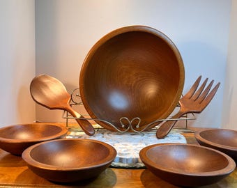 Peut inclure: Un ensemble de saladiers en bois comprenant un grand saladier, quatre petits bols, une cuillère et une fourchette de service en bois. Les bols et les ustensiles sont en bois de couleur chaude, présentés sur un présentoir en métal.
