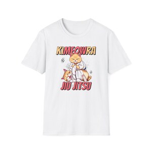 Puede incluir: Camiseta blanca con una ilustración de dibujos animados de dos gatos practicando Jiu Jitsu. El gato superior, con un gi, es naranja y blanco, mientras que el gato inferior es naranja. El texto "Kimeowra" y "Jiu Jitsu" está estilizado.