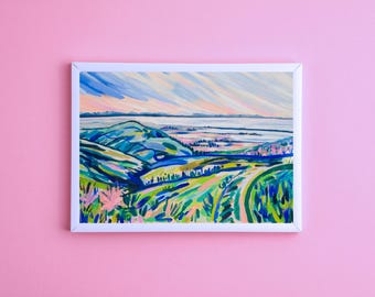 May include: A colorful abstract painting of a landscape with rolling hills, a body of water, and a sky with streaks of blue, pink, and yellow. The painting is framed in white.