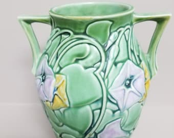 May include: A green ceramic vase with two handles and a floral design. The vase is decorated with a pattern of morning glories in shades of purple, yellow, and green.