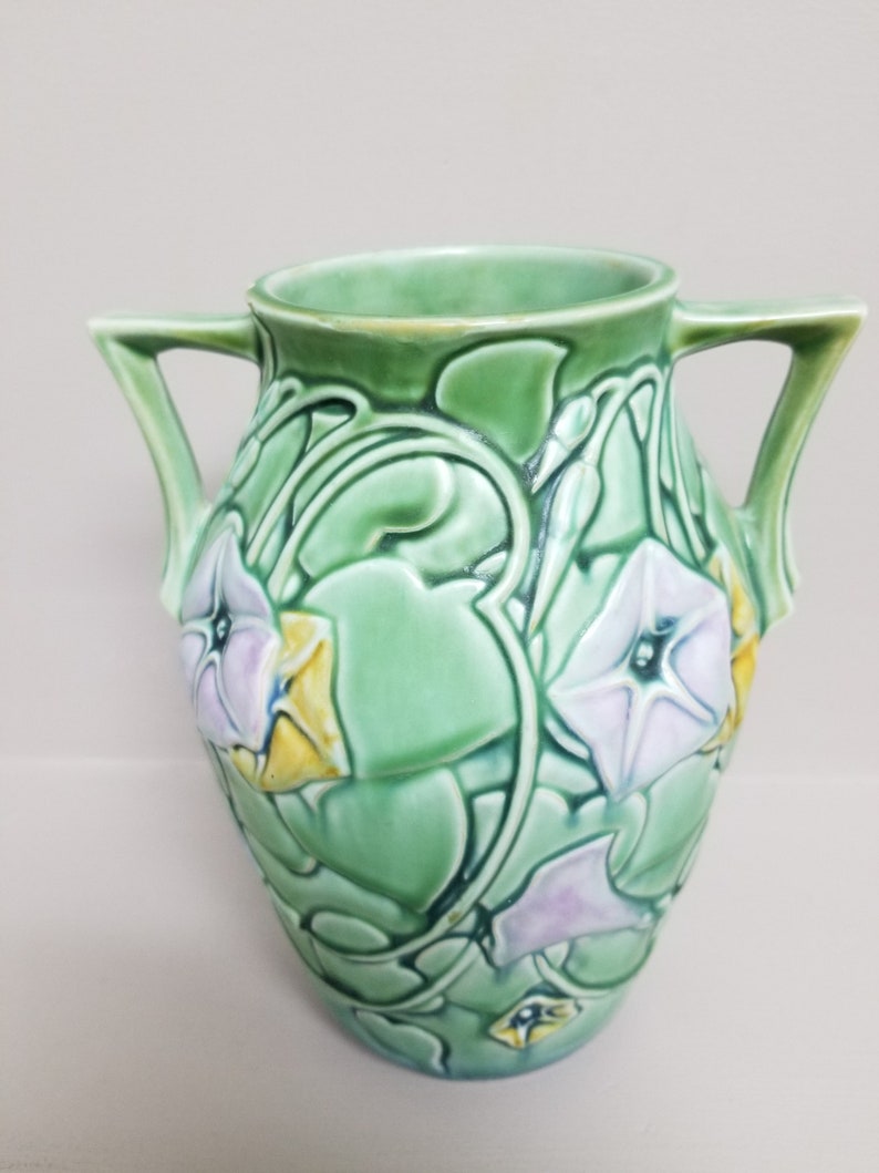 May include: A green ceramic vase with two handles and a floral design. The vase is decorated with a pattern of morning glories in shades of purple, yellow, and green.