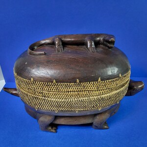 May include: A wooden box shaped like a turtle with a carved lizard on top. The box is made of dark wood and has a woven lid.
