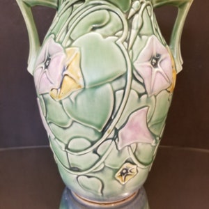 May include: A green ceramic vase with two handles and a floral design. The vase is decorated with pink and yellow flowers and green leaves.