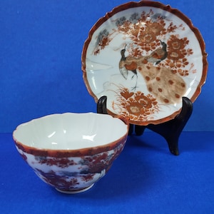 Peut inclure: Un ensemble de bol et d'assiette en porcelaine blanche avec un motif de paon. L'assiette a un bord festonné et une bordure marron. Le bol et l'assiette présentent une peinture détaillée de paons et d'éléments floraux dans des tons de marron et d'orange.
