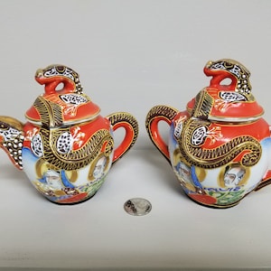 May include: A set of two red and gold teapots with dragon and floral designs. The teapots have lids with a dragon finial.