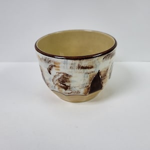 Può includere: Una piccola ciotola in ceramica bianca con disegni astratti marroni e beige. La ciotola ha una forma arrotondata e un bordo leggermente svasato.