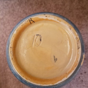 May include: The bottom of a blue and white ceramic vase with a brown rim. The bottom of the vase has a mark that reads "R" and a number "1".