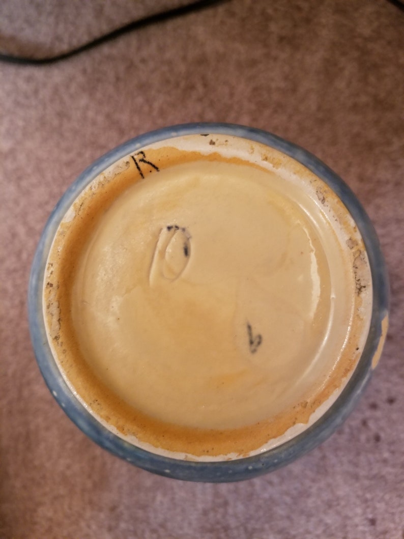 May include: The bottom of a blue and white ceramic vase with a brown rim. The bottom of the vase has a mark that reads "R" and a number "1".