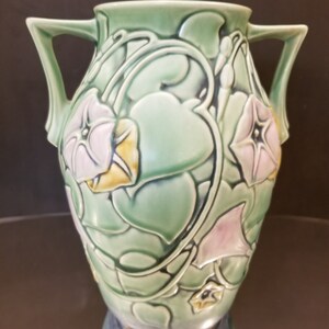 May include: A green ceramic vase with two handles and a floral design. The vase is decorated with pink and yellow flowers and green leaves.
