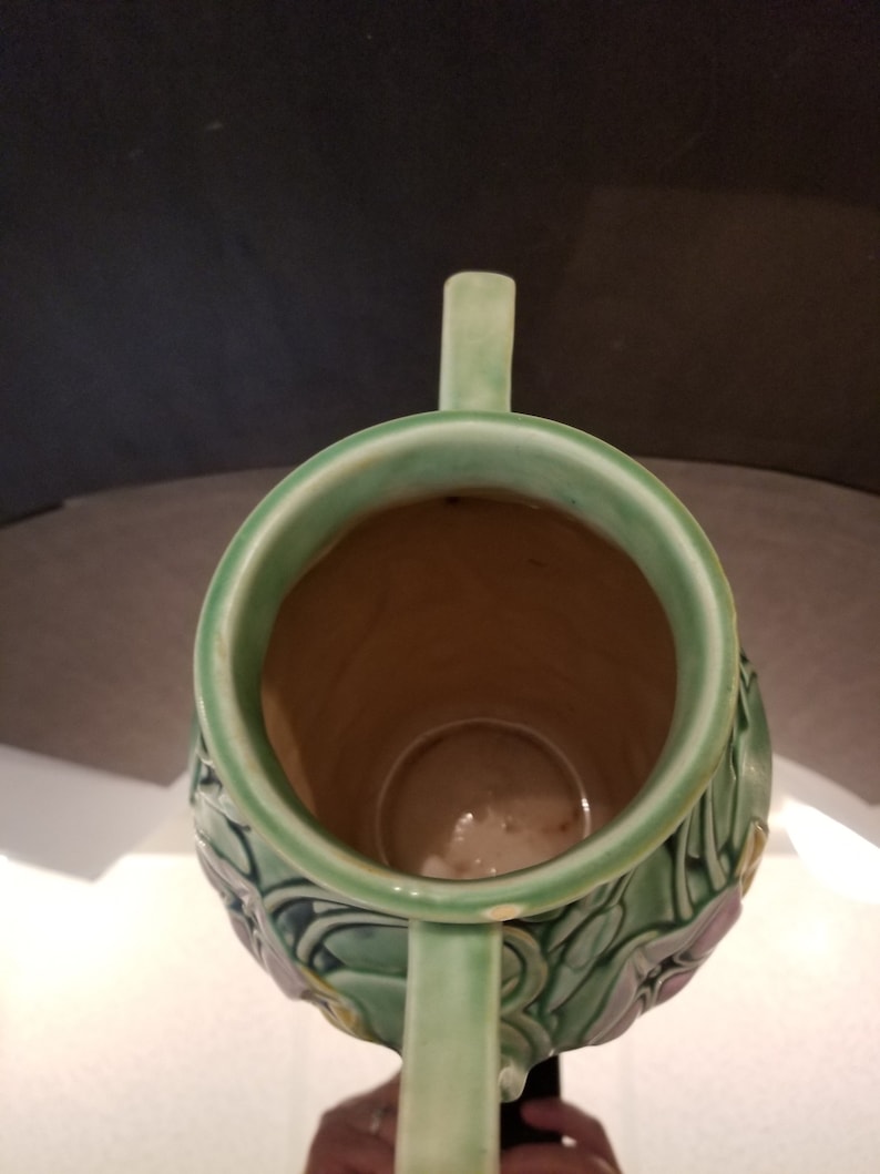 May include: A green ceramic vase with two handles and a floral design. The vase has a wide mouth and a narrow base.