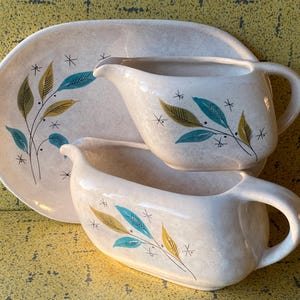 Peut inclure: Un ensemble de service vintage crème comprenant un plat et deux saucières. Chaque pièce est ornée d'un motif botanique en bleu sarcelle, or et vert olive. L'ensemble a une finition mouchetée et des accents d'éclats d'étoiles.