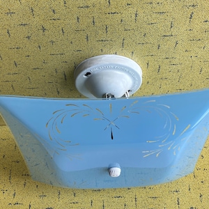May include: A square light blue glass ceiling light fixture with curved sides and a white circular base. The glass features a gold painted leaf-like pattern and a small white knob in the centre. The white base has text reading THE HAZARD CAUTION.