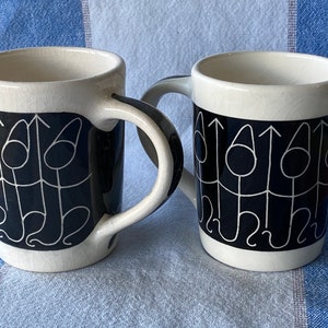 Pode incluir: Duas canecas de cerâmica branca com desenhos abstratos em preto e branco. As canecas têm um fundo preto com linhas e círculos brancos.