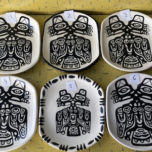 Pode incluir: Seis pratos de cerâmica branca com desenhos estilizados em preto e branco de um pássaro com rosto humano. Os pratos são numerados de 1 a 6.