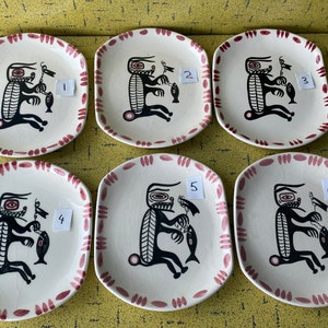 Pode incluir: Seis pratos de cerâmica branca com borda vermelha e um desenho em preto e branco de um animal estilizado segurando um peixe. Os pratos são numerados de 1 a 6.