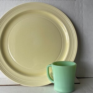 Può includere: Un grande piatto da cena in ceramica giallo con un bordo rialzato e una tazza di vetro verde più piccola.