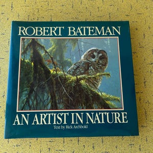 May include: A hardback book titled Robert Bateman An Artist in Nature with text by Rick Archbold. The dark green cover features a central rectangular illustration of a brown owl perched on a mossy tree branch within a forest setting.