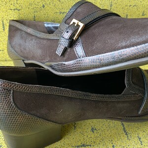 May include: A pair of brown suede heeled shoes with a buckle detail. The shoes have a snakeskin-like texture on the toe and heel.