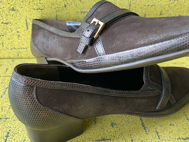 May include: A pair of brown suede heeled shoes with a buckle detail. The shoes have a snakeskin-like texture on the toe and heel.