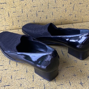 May include: A pair of black patent leather shoes with a fabric upper. The shoes have a low block heel.