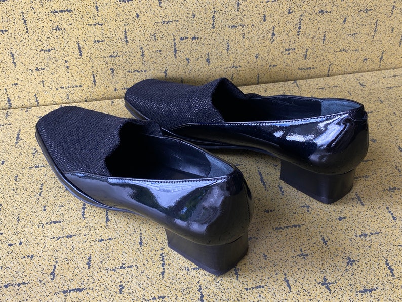 May include: A pair of black patent leather shoes with a fabric upper. The shoes have a low block heel.